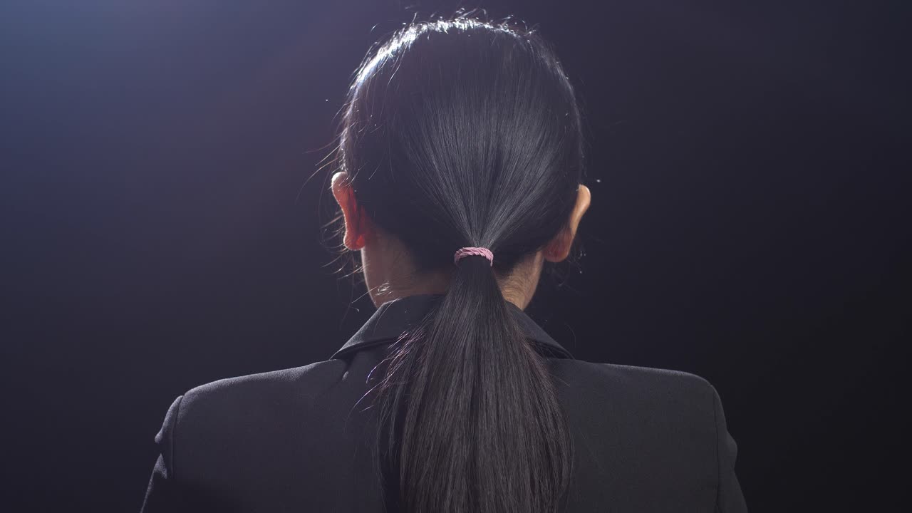 블랙 스크린 스튜디오에서 말하는 비즈니스 슈트를 입은 아시아 스피커 여성의 뒷면