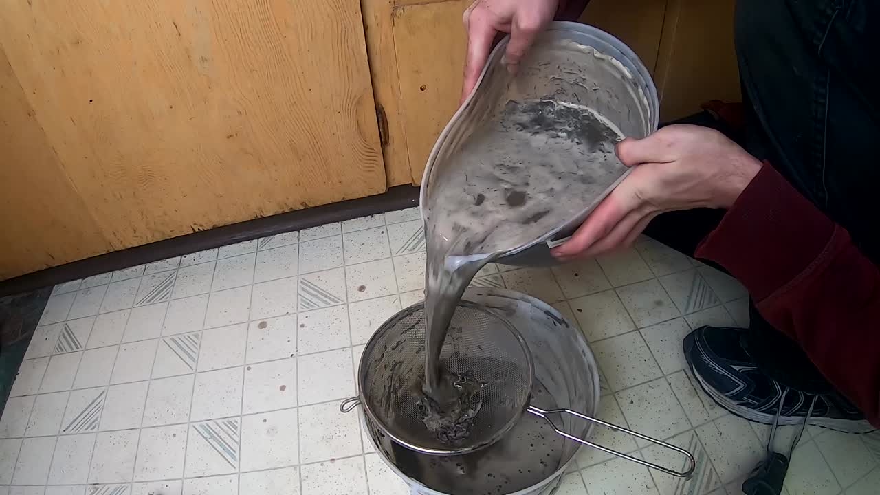 Using two plastic buckets and a strainer to strain clay from mud and ...
