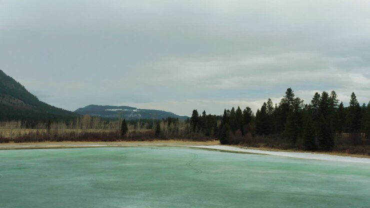 Bright teal glacial water lake with sandy shore surrounded by mountains and woods