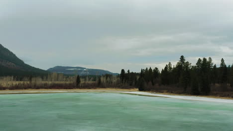 Lago-De-Agua-Glacial-Verde-Azulado-Brillante-Con-Orilla-De-Arena-Rodeada-De-Montañas-Y-Bosques