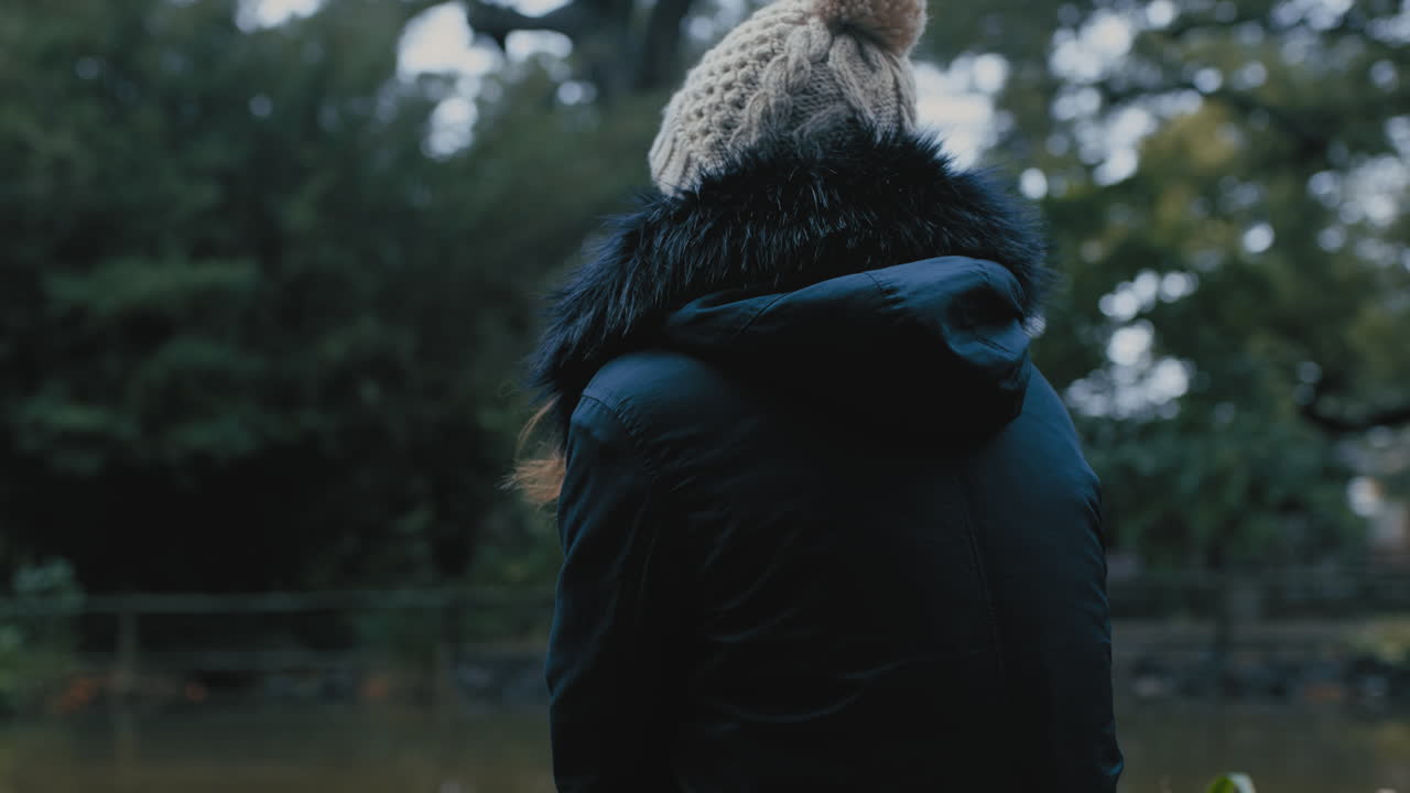mujer joven sentada sola en el parque disfrutando de un estanque de naturaleza tranquila adolescente solitaria sintiéndose deprimida en un día frío y nublado
