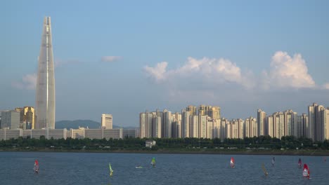 Un-Grupo-De-Hombres-Practica-Windsurf-En-El-Río-Han-Cerca-De-La-Torre-Lotter-Durante-El-Día,-Distrito-Jamsil-De-La-Ciudad-De-Seúl,-Corea-Del-Sur