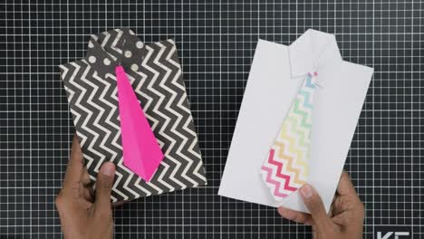 Two-hands-holding-shirt-shaped-gift-cards-with-patterned-ties-on-a-grid-background