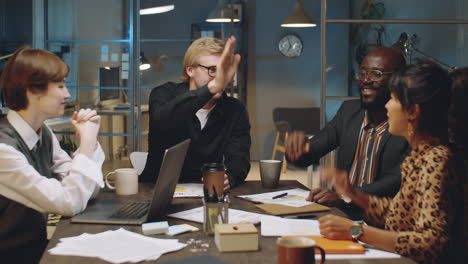 business team talking and high fiving at night office meeting