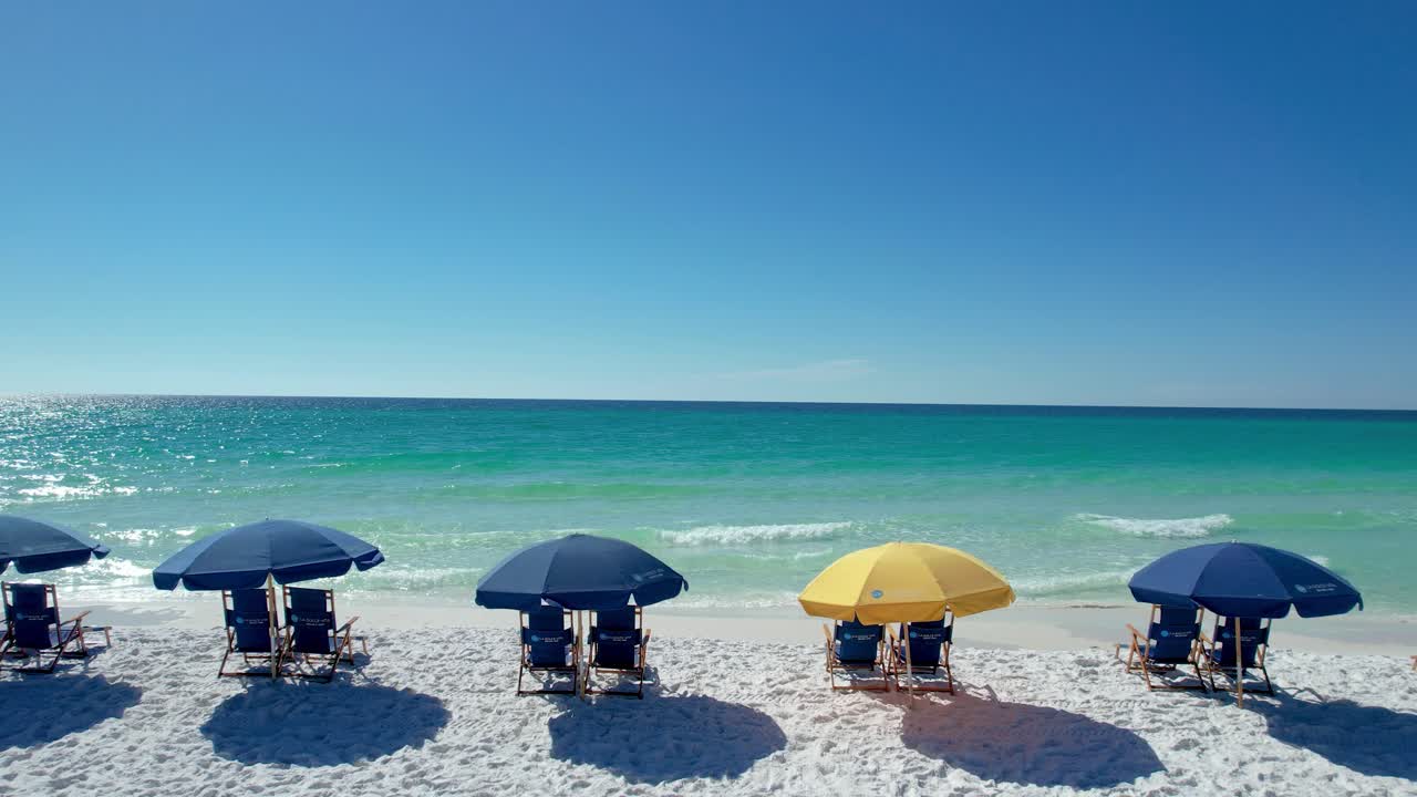 Blue umbrellas on Destin Beach gulf coast panhandle Florida white sandy beach clear emerald waters fly over with drone aerial view bright sunny day