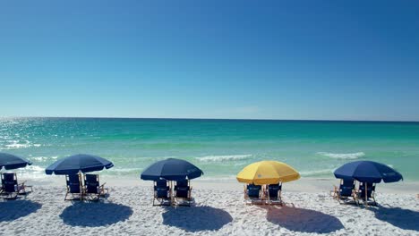 blue umbrellas on destin beach gulf coast panhandle florida white sandy beach clear emerald waters fly over with drone aerial view bright sunny day