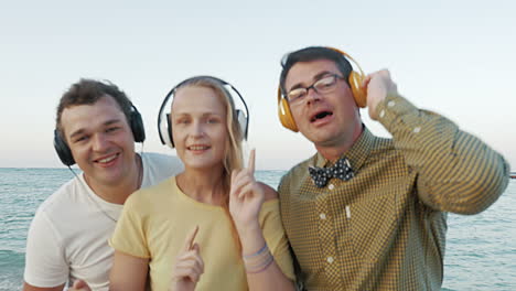 excited trio enjoying music in headphones outdoor