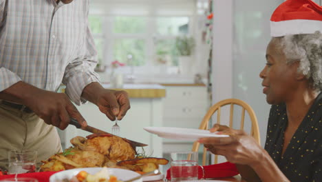 grandfather carving and serving as multi generation family enjoy eating christmas meal at home