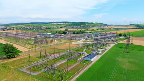 aerial view of electric substation industry - high voltage towers in scenic fields - drone shot