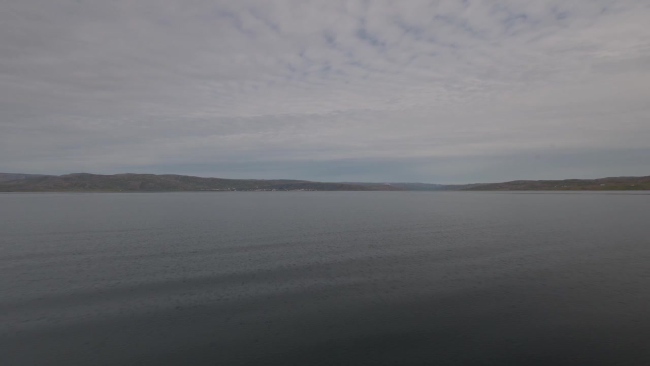 A peaceful wide shot of the dark, still ocean waters in a fjord near Holmavik, Iceland, featuring distant hills and a cloudy sky.