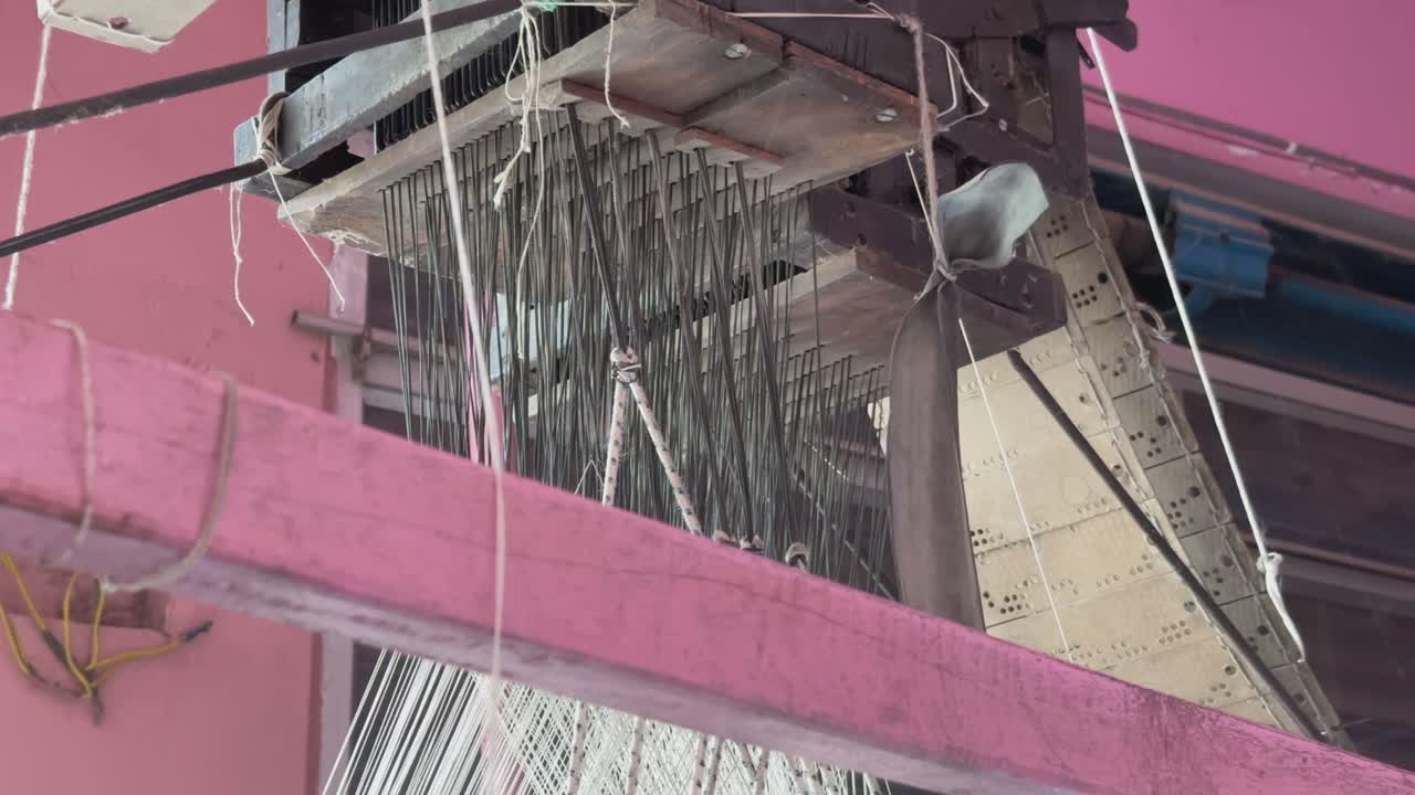 Closeup threads are being raised or lowered to create intricate designs on fabric in traditional handloom process