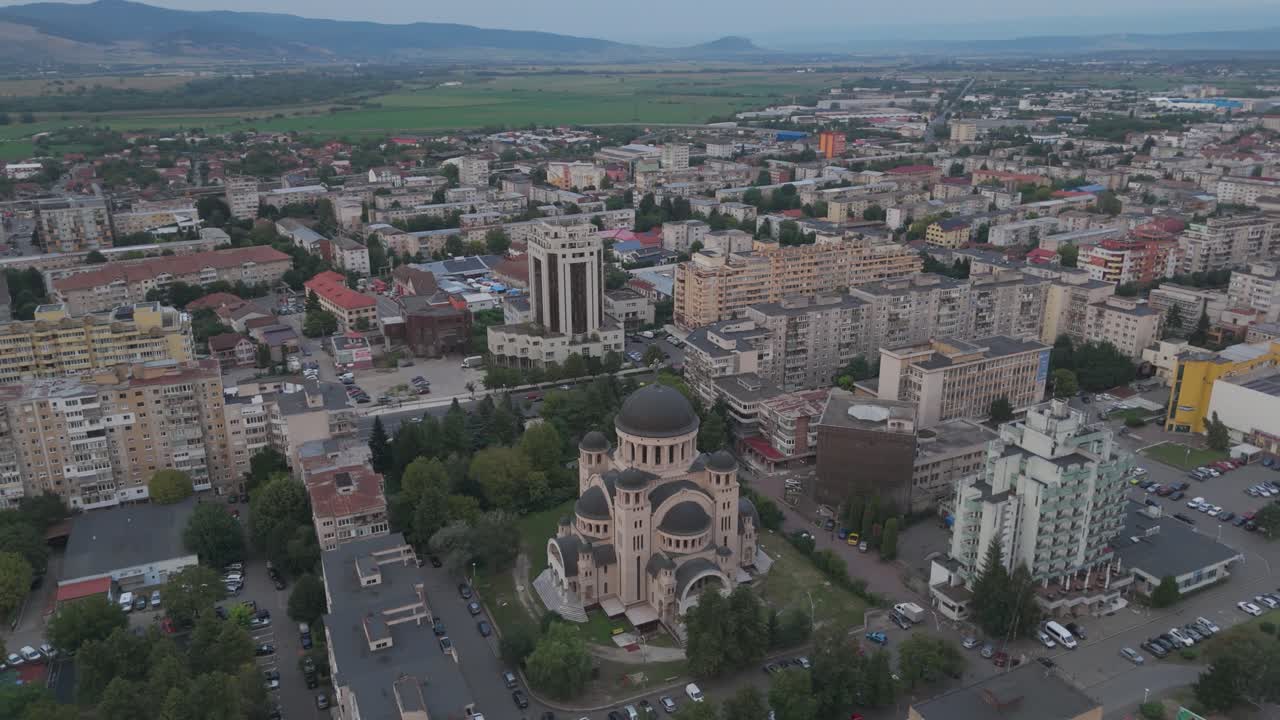 Aerial dusk view of Catedrala Adormirea Maicii Domnului with the softly lit Deva cityscape behind it