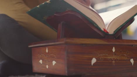 primer plano de una copia abierta del corán en un stand en casa con un hombre recitando o leyendo 2