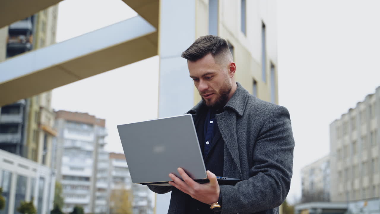 Businessman with a laptop outdoors. Handsome man in warm coat standing in the city street and working on a laptop. Business and work concept.
