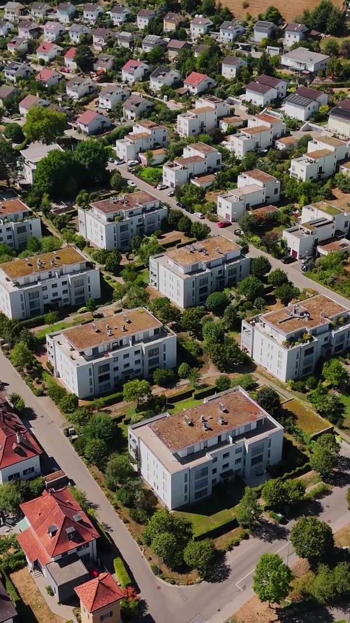 Vertikale Luftaufnahme eines Wohnviertels in der Schweiz mit Wohnblöcken, Einfamilienhäusern, baumgesäumten Straßen, Gärten und organisierter Vorstadtbebauung
