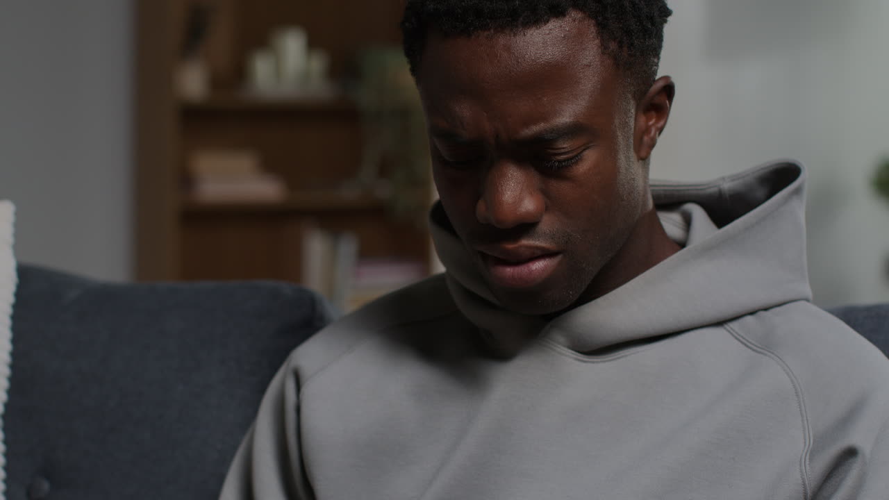 Close Up Of Unhappy And Depressed Young Man Sitting On Sofa At Home Looking At Mobile Phone 3