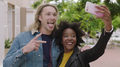 portrait of attractive young multi ethnic couple posing enjoying taking selfie photo using smartphone making faces lively urban youth