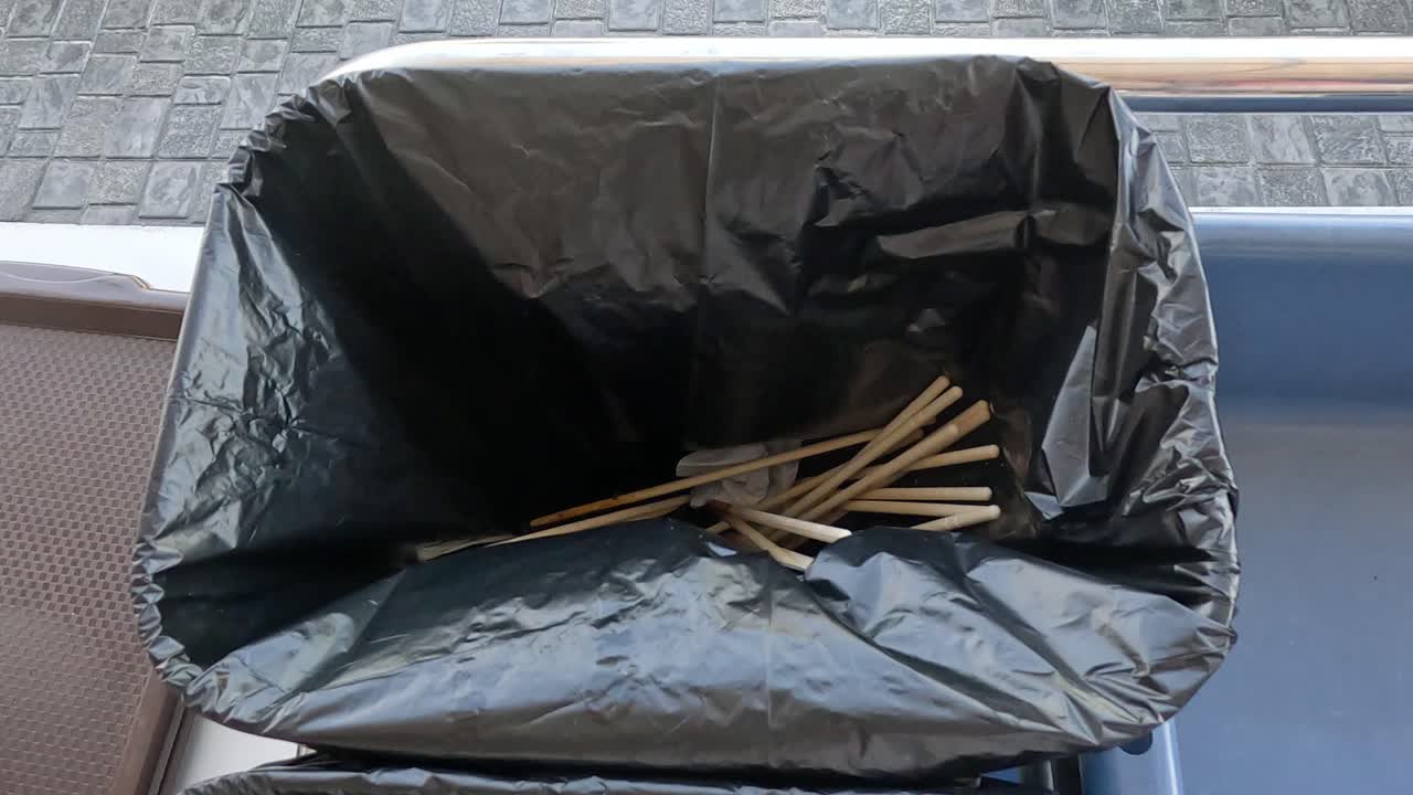 Hand discarding chopsticks into a lined trash bin