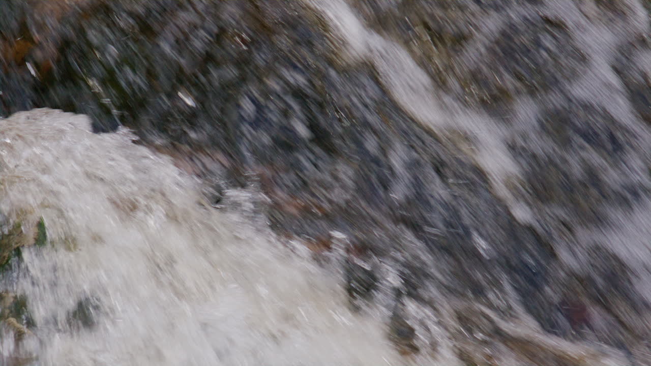 Abstract motion of rushing water veiling stone texture in a vertical flow from a slow-motion waterfall closeup