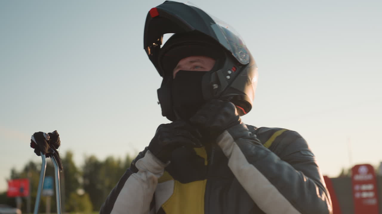 Biker puts on helmet preparing for ride with bright sunlight creating glowing atmosphere around him wearing protective leather jacket symbolizing safety power freedom