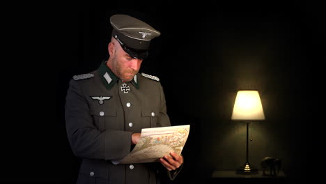 un oficial alemán del ejército wehrmacht de la segunda guerra mundial leyendo un mapa en una habitación oscura con una lámpara