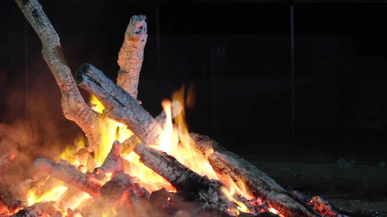 Close-up of glowing bonfire logs burning intensely at night. Ideal for camping, survival scenes, cinematic fire transitions, outdoor heat or ambient fireplace visuals.