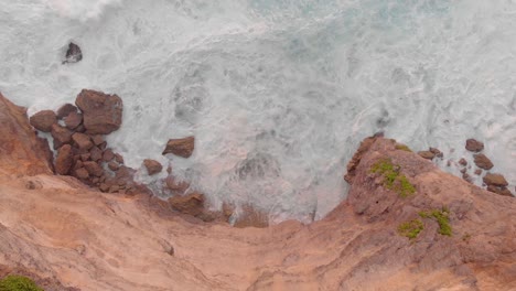 Cinematic-smooth-aerial-drone-shot-of-large-waves-crashing-into-huge-cliff-edge-in-uuwatu,-Bali-during-golden-hour-on-summer-sunset