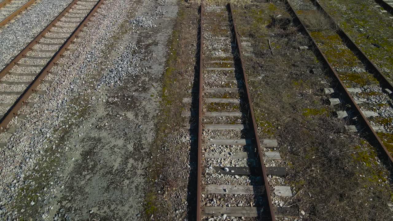 aerial drone footage gliding and glying over and along rusty brown metallic traintracks or railroad tracks in Tallinn Väike train station during a sunny day in Tallinn Estonia. Brown overgrown grass.