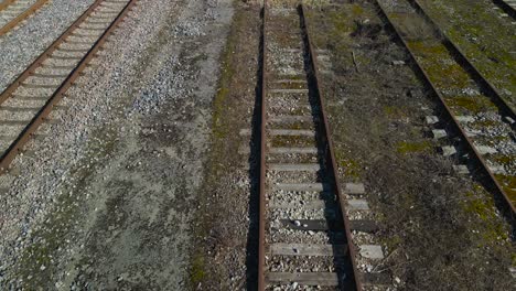 aerial drone footage gliding and glying over and along rusty brown metallic traintracks or railroad tracks in Tallinn Väike train station during a sunny day in Tallinn Estonia. Brown overgrown grass.