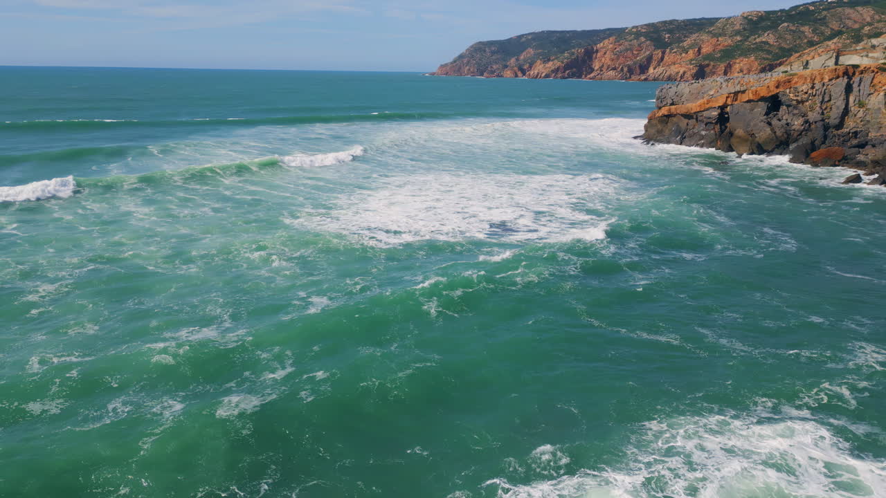 Blue ocean waves rolling to stone shoreline. Aerial sea water washing cliffs.