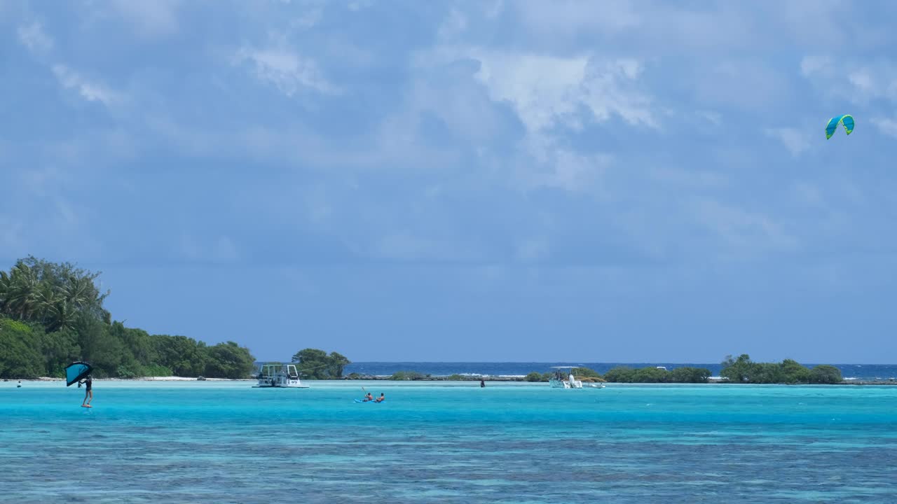 Water sports of foil surfing, kayaking, and tour boats in lagoon on tropical island of Moorea in French Polynesia, South Pacific