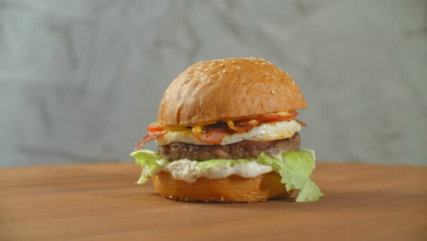 gran hamburguesa con carne de res, chuleta, tomates, setas y pepinos con queso derretido gira en una tabla de madera sobre un fondo claro.