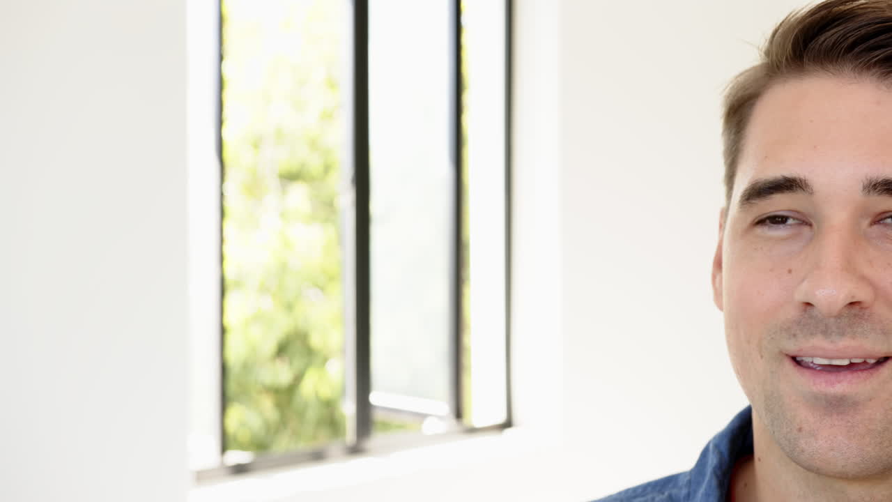 Smiling man in casual shirt standing near window with natural light, at home, copy space
