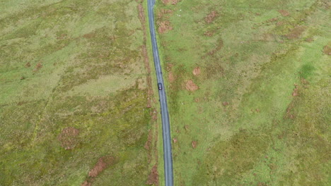 Aerial-view-following-a-black-car-traveling-along-a-country-road,-in-the-English-Lake-District