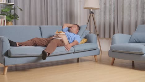 full body of a fat asian man sleeping while having french fries with ketchup eating fast food on a sofa in the living room at home