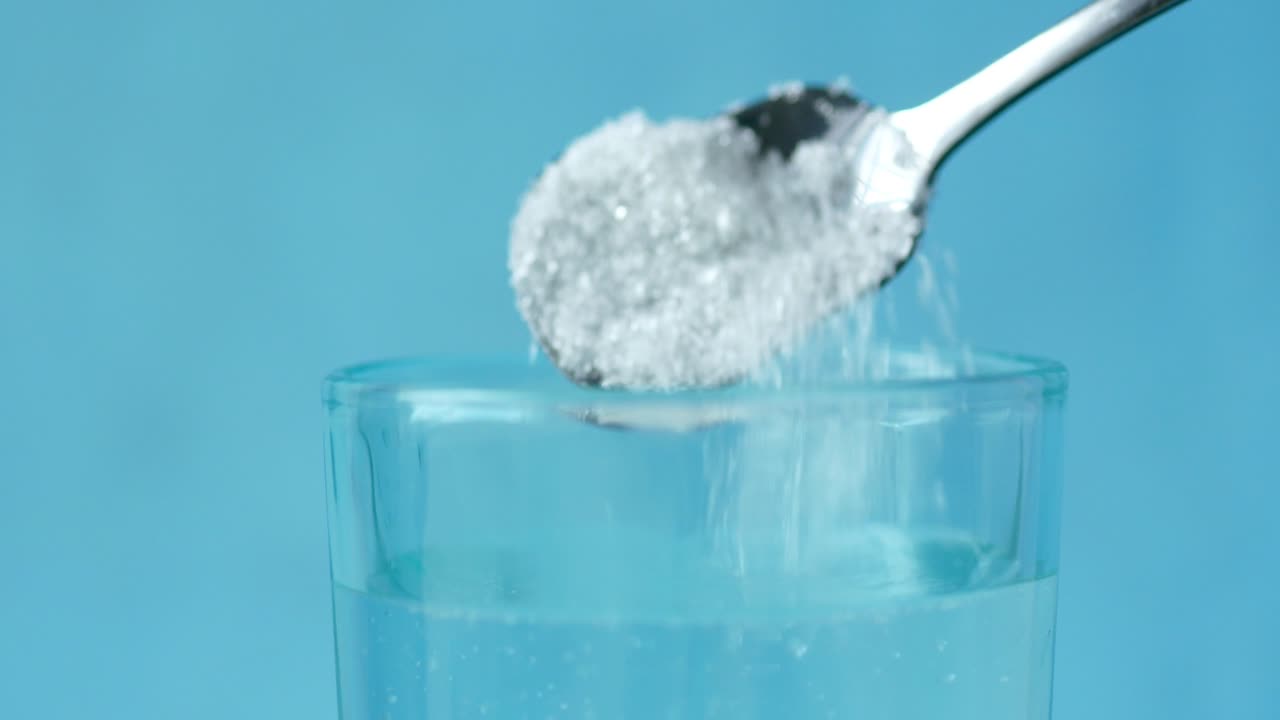 vertiendo azúcar blanca en un vaso de agua en la mesa ,