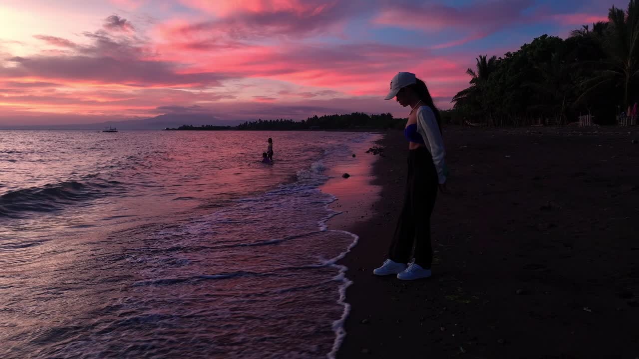 Silhouette of Woman enjoying purple sunset at beach in Philippines. Aerial orbit shot.