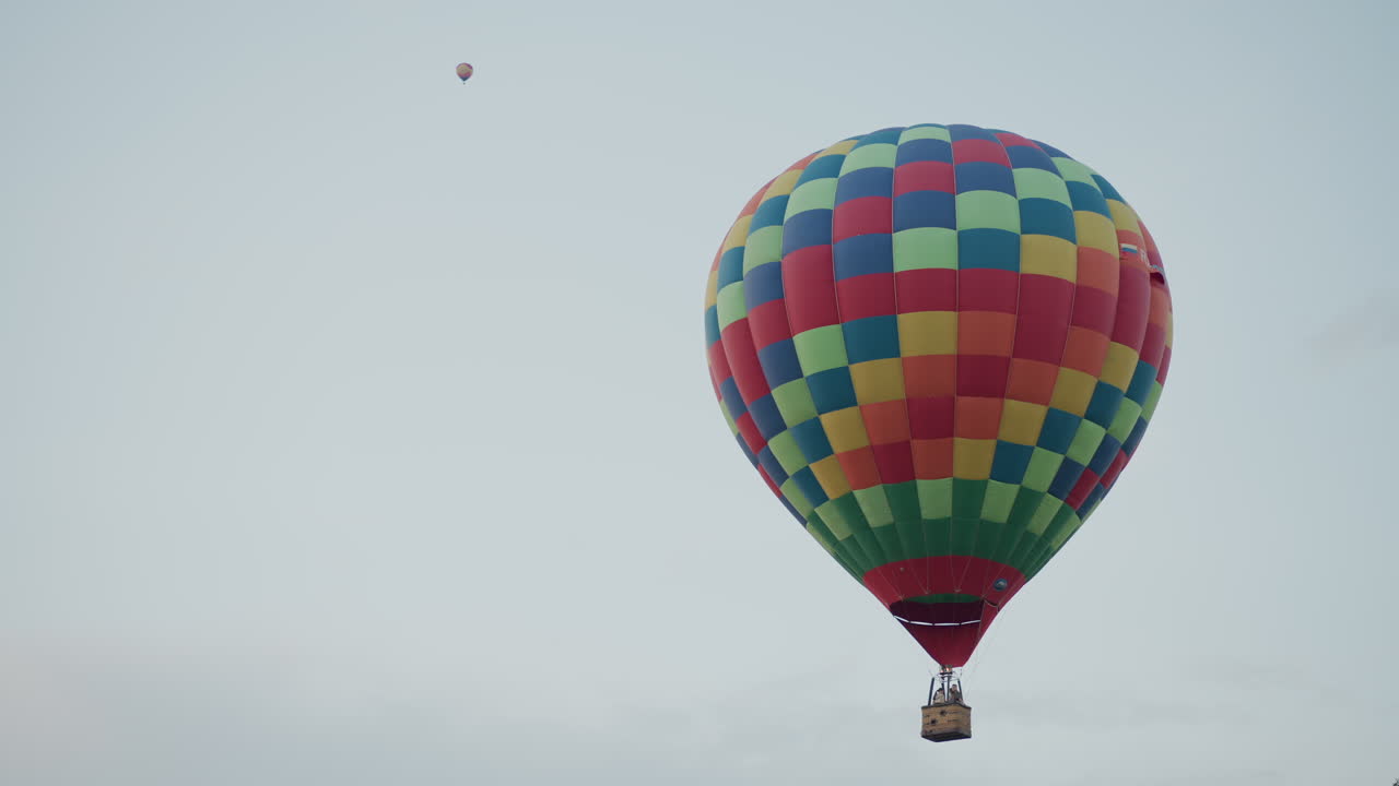 two hot air balloons carrying passengers ascending slowly against pastel sky over field and tree line at dusk capturing aerial adventure with burner flame visible near basket