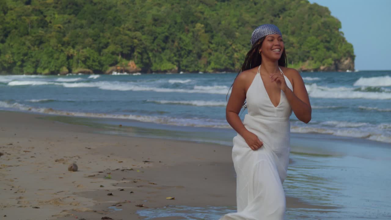 una mujer corriendo en la playa con un vestido blanco de playa y el pelo ondeando al viento con las olas del mar rompiendo en la costa