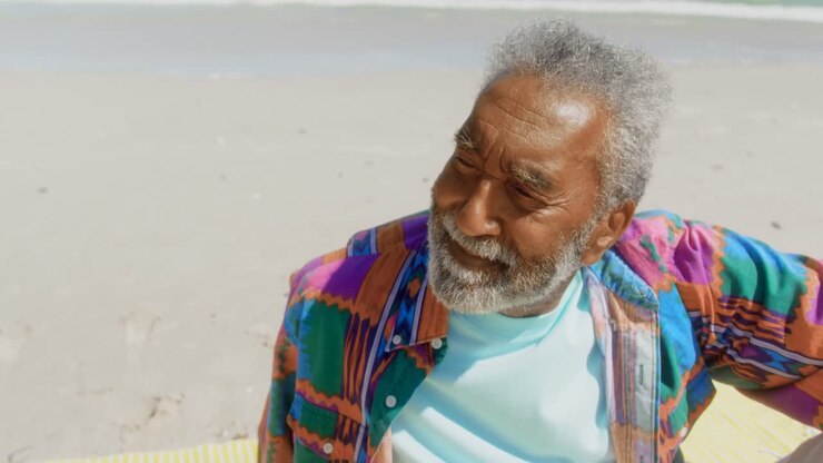 Front view of thoughtful active senior African American man relaxing on beach in the sunshine 4k