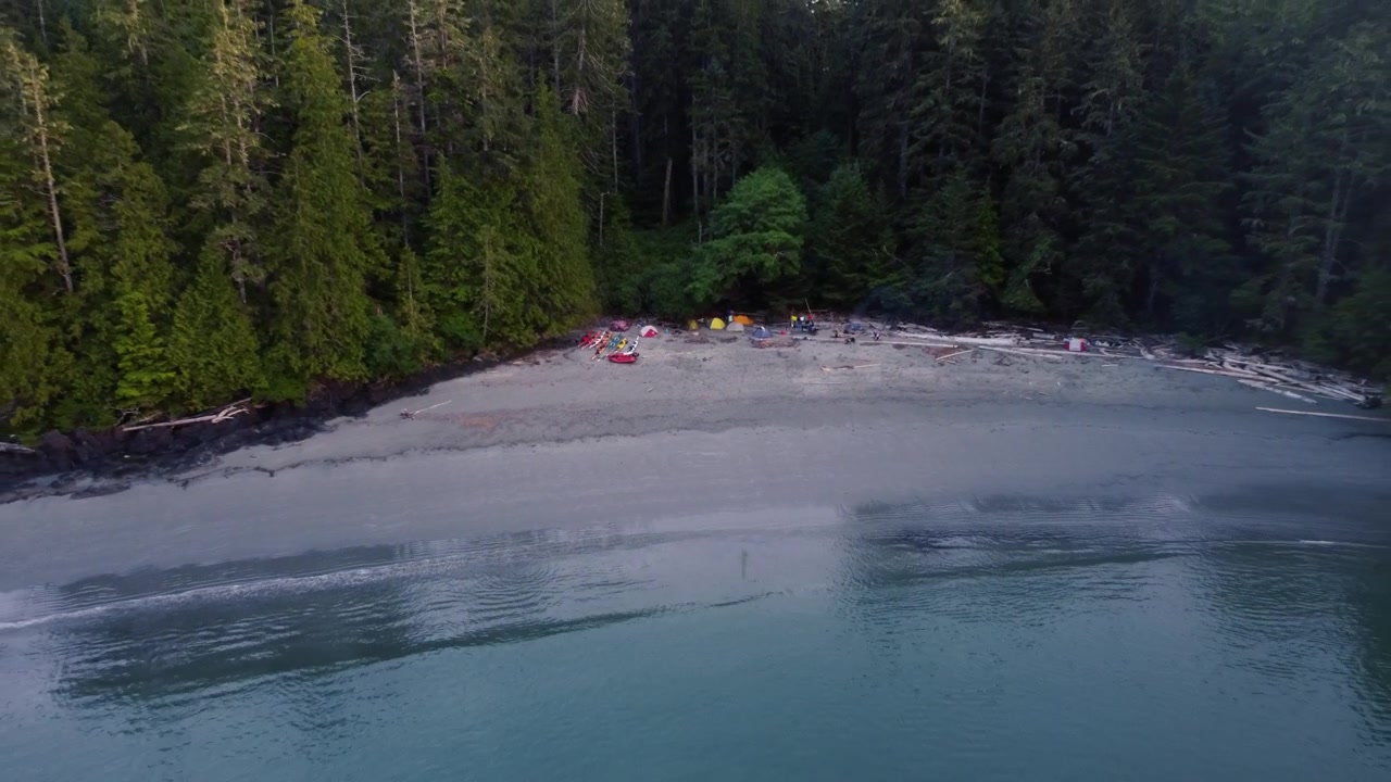 Splendido campeggio sulla spiaggia con ripresa drone in allontanamento che rivela l'oceano e l'isola.