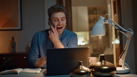 laughing startuper calling cellphone talking with smile at late home closeup
