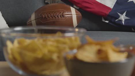 salón en casa de la persona que ve el partido de fútbol americano en la televisión con bebidas, bocadillos y pelota 4