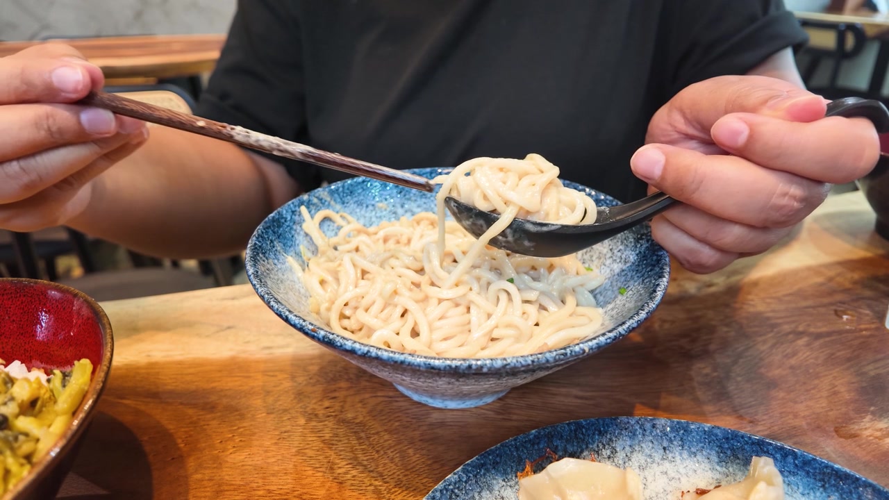 Primo piano di mani che usano le bacchette per mettere i noodles in un cucchiaio a Bangkok, Thailandia