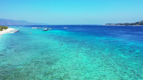 Crystal-emerald-water-of-calm-turquoise-lagoon-with-boats-floating-near-shore-of-tropical-island-with-white-beach-in-Indonesia