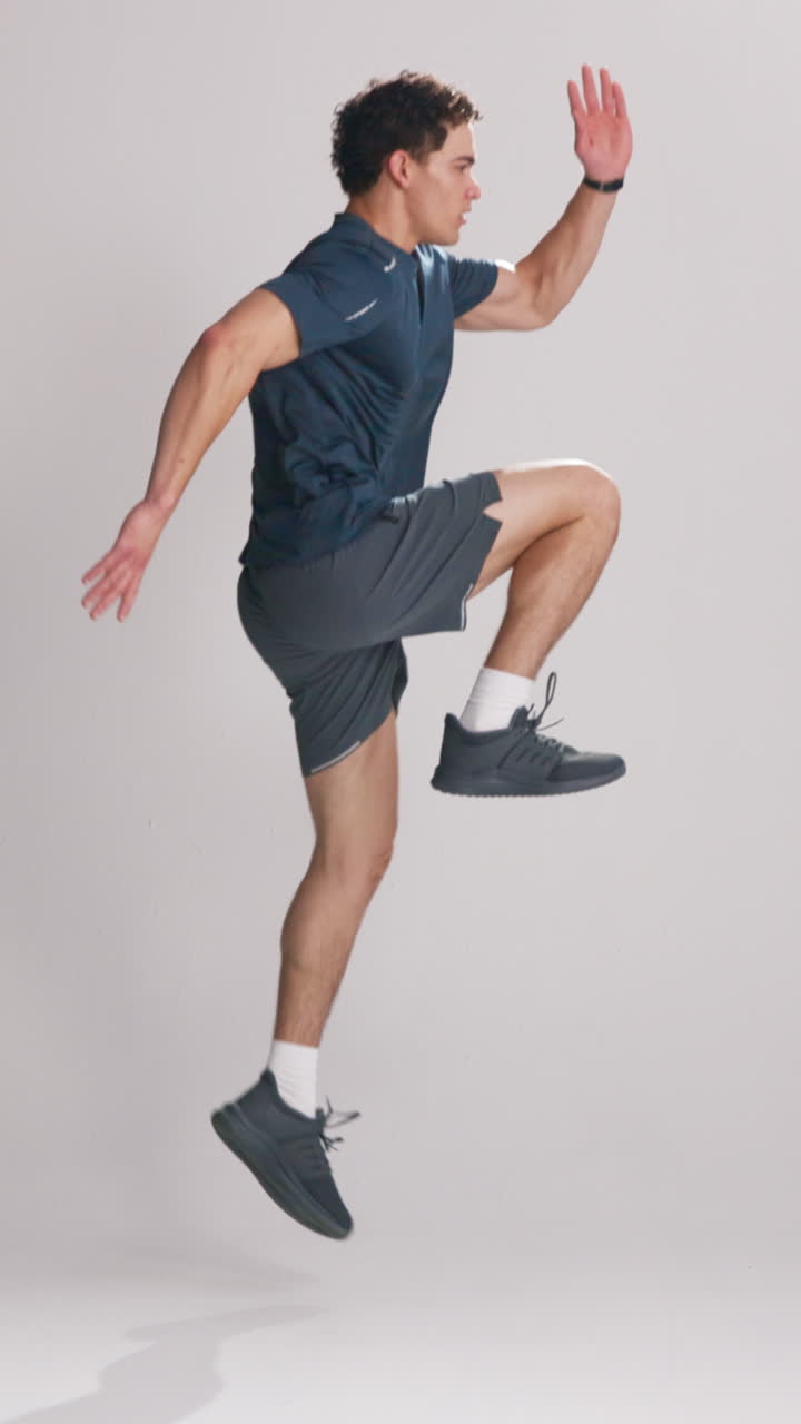 Giovane uomo che esegue esercizio di salto a ginocchia alte in studio.