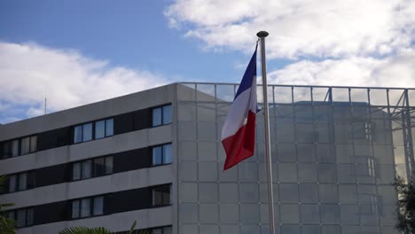 French-flag-on-low-wind-in-front-of-modern-office-building-in-France,-Stable-medium-shot