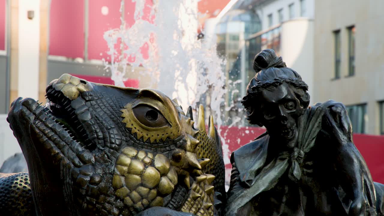 Brass creature and human sculpture fountain splashes water in city center, daylight, static shot