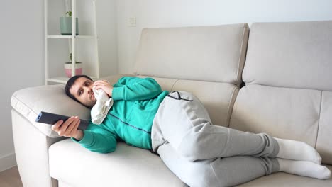 White-man-lying-on-sofa-icing-his-jaw-and-excitedly-watching-television