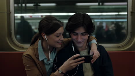 young couple sharing earphones and watching a smartphone on a subway